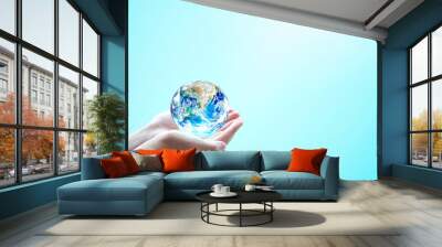 Human hands hold globe on blurred blue nature background. Elements of this image furnished by NASA Wall mural