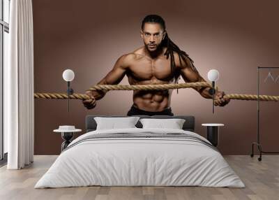 Muscular African American Black athletic fitness model wearing red underwear  holding a thick rope with six pack abs in studio with dramatic lighting against a brown background   Wall mural