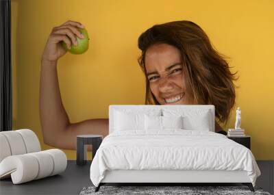 Powerful young fit woman holding an apple showing on a solid yellow background Wall mural