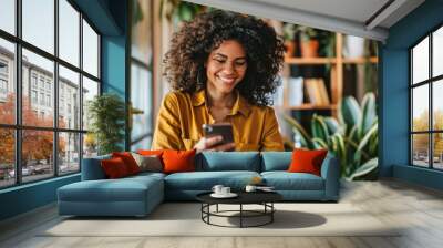 Young woman with curly hair using a mobile phone and laptop at home Wall mural