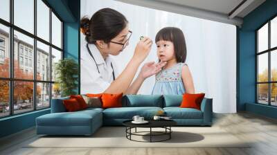 Asian doctor woman examine eyes of little asian girl in the clinic.  Senior looks in instrument for checking eyes at ophthalmologist. Health care and medical for young toddler kid concept. Wall mural