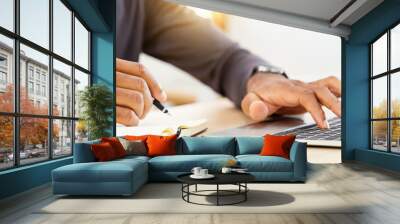 Closeup businessman hand holding pen writing on notebook, work on laptop computer in modern office. Student lecturing while studying online internet course. Write on journal diary panoramic banner Wall mural