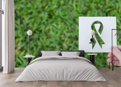 Hands holding cut paper with logo of ribbon over green glass background. Symbol icon for breast cancer awareness. Healthcare and medical spring concept banner Wall mural