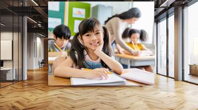 Portrait of smile little pupil writing at desk in classroom at the elementary school. Student girl doing test in primary school. Children writing notes in classroom. Education knowledge concept Wall mural