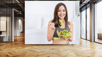 Portrait of young beautiful asian girl in sportswear holding a glass bowl of salad fork in her hands. Concept of vegan woman eating healthy food and tasty food health care medical plant base concept. Wall mural