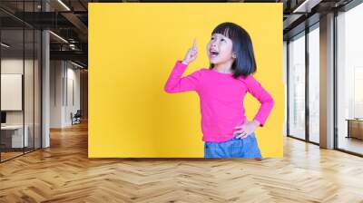 Portrait of young little asian girl hand point up isolated on yellow background with copy space. Education for toddler or preschool, childhood lifestyle back to school concept Wall mural