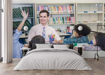 Pupils studying with teacher in group study classroom, Teacher and little children sitting lift their hands up. Home school back to school concept. Wall mural