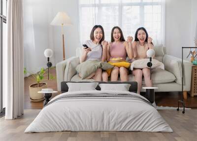 Young group of asian girls friend holding remote control watching TV series show.Beauty cheerful woman teenage sitting on sofa couch having fun relax leisure time at home. Stay home activities. Wall mural