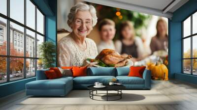 smiling old woman holding juicy roasted turkey for thanksgiving on background of family and table with food, generative AI Wall mural