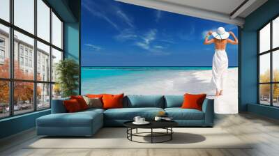 elegant woman in white dress holds sun hat and walks on idyllic beach of maldives, relax in a tropical island Wall mural