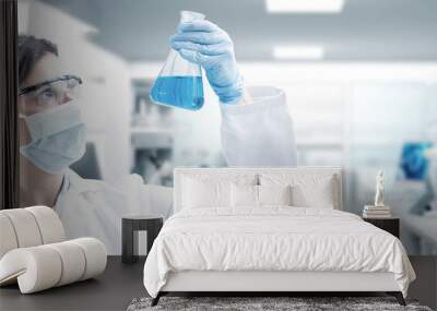 Female scientist measuring blue liquid in a flask at a chemical laboratory. Concept about biochemistry or pharmaceutical research and development.Scientific researcher work. Wall mural