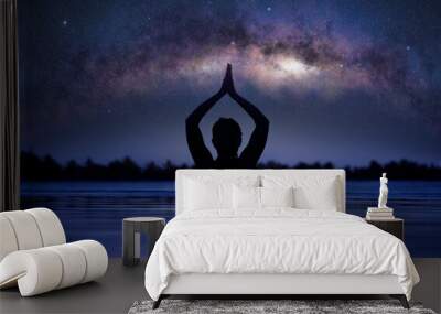 Silhouette of a woman practicing yoga lotus pose in infinity swimming pool under a starry sky with milky way arch Wall mural