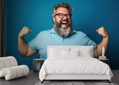 Excited fat man celebrating success. Happy plus size bearded man on blue background Wall mural