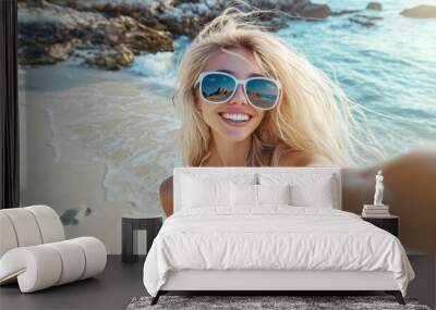 Portrait of smiling young woman taking a selfie at beach during. Cheerful blond woman enjoying at beach during holiday. Happy girl taking photo over exotic tropical beach looking at camera. Wall mural