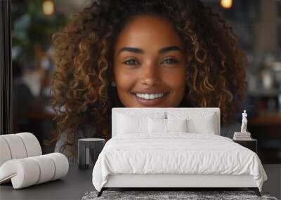 Close up portrait of a beautiful smiling woman with curly hair sitting in a modern office or coffee shop. She is casually dressed Wall mural