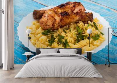 Grilled chicken drumstick and pasta on white plate, blue wooden background Wall mural