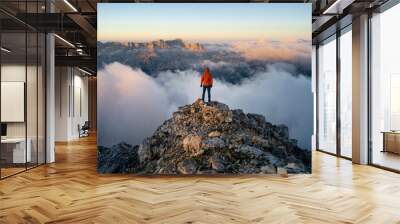 A hiker stands on the ridge watching the valley being flooded by clouds at sunset. Traveling in mountains. Adventure, Art, Travel and Hike concept. Wall mural