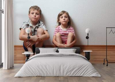 boy and girl in home clothes sit leaning on the wall Wall mural