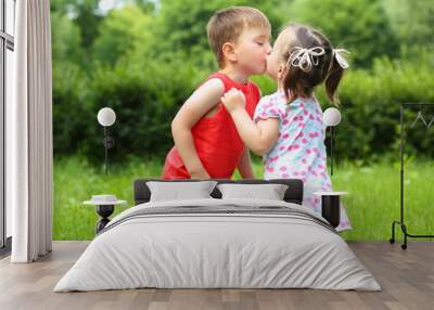 Little girl and boy kiss on fresh green grass in summer sunny park Wall mural