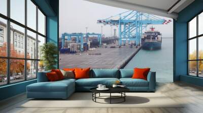 Men load cargo boat docked to industrial port with blue cranes Wall mural