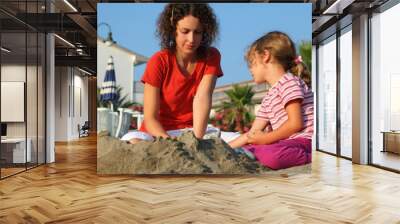 Mother with daughter sit on  beach in  day-time and play on sand Wall mural