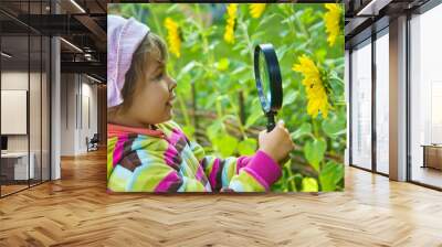 pretty Little Girl with magnifying glass looks at flower Wall mural