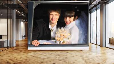 smiling groom and bride with bouquet sitting in limousine Wall mural