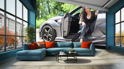 The girl with long black hair sitting in a car with an open door in front of green foliage Wall mural