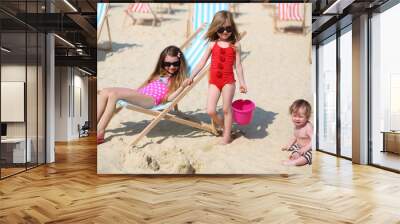 Two little girls in sunglasses and baby on beach at sunny day. Wall mural