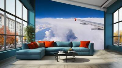 Wing of flying airplane at clouds in blue sky, view from window Wall mural