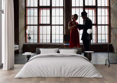 Woman in dress and man in black suit dance tango near big window in room Wall mural