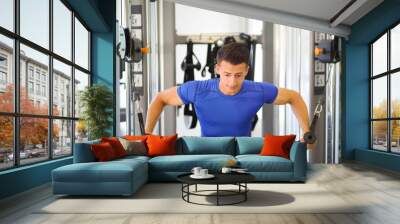 Young slim man does exercises on simulator in modern gym, shallow dof Wall mural