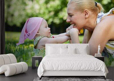 Young smiling mother plays with her baby on grass Wall mural