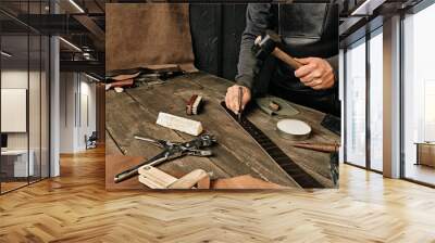 Working process of the leather belt in the leather workshop. Man holding tool. Tanner in old tannery. Wooden table background. Close up man arm. Maintenance concept. Goods production. Wall mural