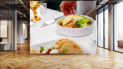 A fresh salad with grilled chicken, greens, and cherry tomatoes served at a well-set dining table. Utensils neatly placed beside the plates, and two glasses—one with an orange beverage—are visible. Wall mural