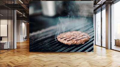 A sizzling burger patty cooks on a grill, smoke rising from its perfectly seared surface. Grill marks accentuate its juiciness. Wall mural