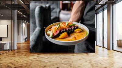 Close-up of a person holding a plate of colorful, gourmet food in a restaurant setting. Wall mural