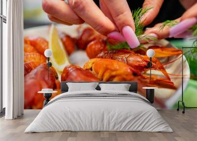 Close-up of hands garnishing a plate of cooked crayfish with fresh dill and a lemon slice. Perfect for culinary themes, seafood preparation, and gourmet presentations. Wall mural