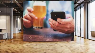 close up of man hand hold smartphone, drinking beer and reading message at bar or pub Wall mural