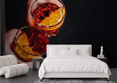 Close up of mens and women's hands clinking the glasses with Negroni cocktails on a black background. Wall mural