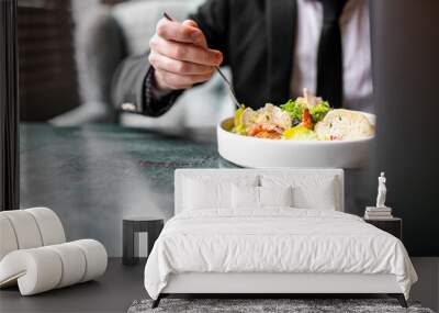 person savoring a fresh salad at a stylish green table. The individual, dressed in formal attire, uses a fork to enjoy the colorful mix of leafy greens, vegetables, and bread. Wall mural