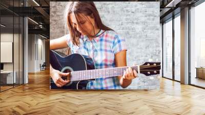 portrait of young teenager brunette girl with long hair playing an black acoustic guitar on gray wall background Wall mural