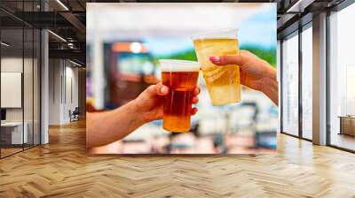 two plastick cup of beer in man and woman hands. Beer clinking outdoor Wall mural