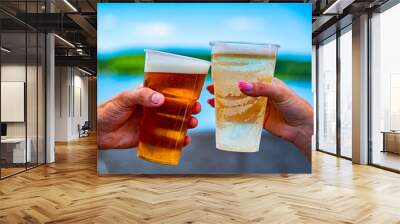 two plastick cup of beer in man and woman hands. Beer clinking outdoor Wall mural