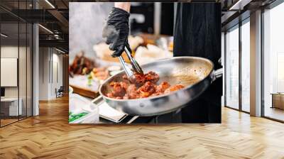 woman chef cooking chicken wings in a sauce in the kitchen Wall mural