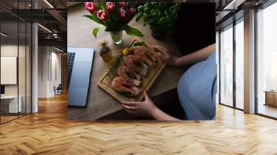 The pregnant girl is watching the show and preparing salmon with rosemary and lemon for lunch. on the table are fresh tulip flowers Wall mural