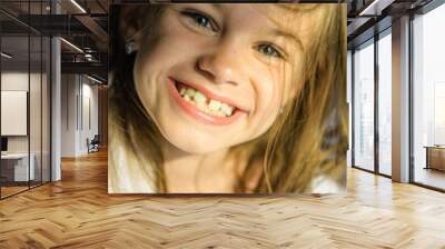 Сute little girl is smiling funny at the camera. The gap between the teeth. Funny and beautiful smile. Beloved daughter. Crooked baby teeth in a funny girl Wall mural