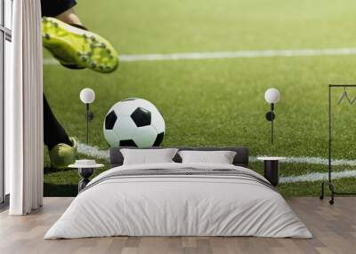 Foot of a child football player and ball on the football field, kicking a corner kick Wall mural