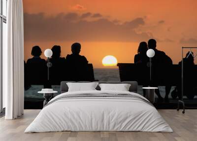 Silhouette of a group of people who sits on the bench, looking at the sunset Wall mural