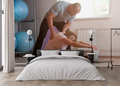 Coach man helps an elderly woman to stretch the body during training in the gym. Healthy lifestyle concept Wall mural